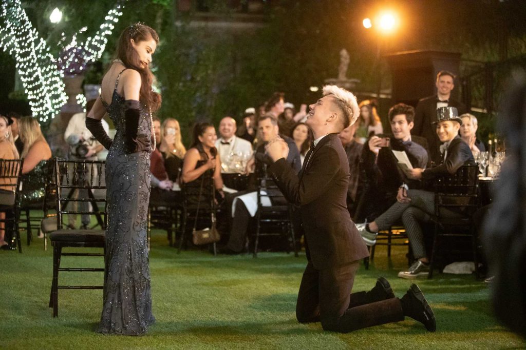 An man in a suit kneels down in front of an elegantly-dressed woman at an immersive theater event